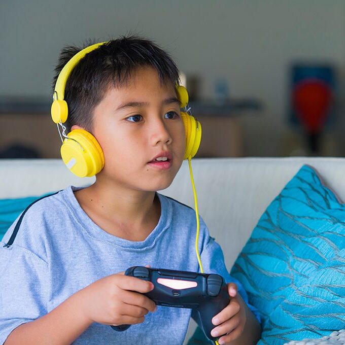 portrait of young little kid excited and happy playing video game online with headphones holding controller enjoying having fun sitting on couch